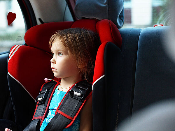 Ein Kind sitzt im Kindersitz eines Autos und schaut aus dem Fenster.