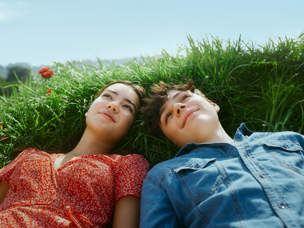 Junge und Mädchen liegen nebeneinander im Gras und blicken in den Himmel.