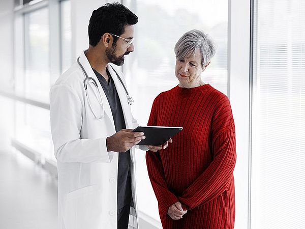Eine ältere Dame spricht mit einem Arzt während beide auf ein Tablet schauen
