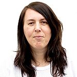 Eine Frau mit dunkelbraunen schulterlangen Haaren blickt in die Kamera. Sie trägt ein weißes Oberteil und steht vor einem weißen Hintergrund.