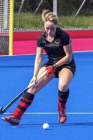 Eine Frau in Sportbekleidung spielt Floor Hockey. Sie hält dabei einen Schläger in der Hand und schießt einen Ball