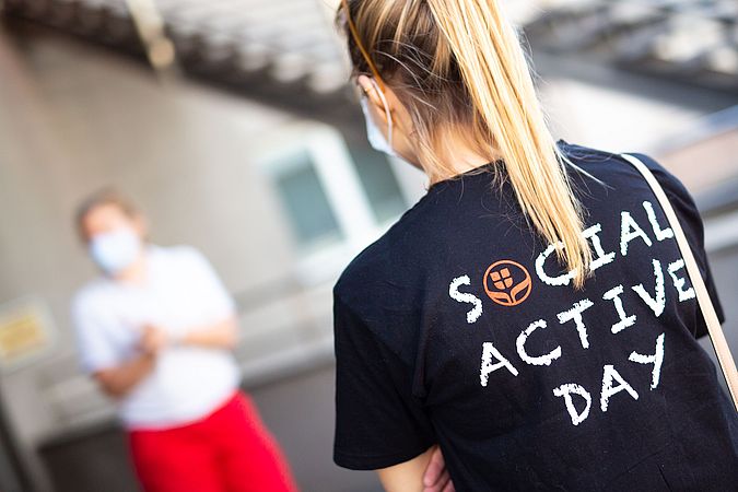 Bild zeigt Frau mit Zopf mit einem Social Active Day Shirt. Sie leistet freiwillig soziales Engagement.