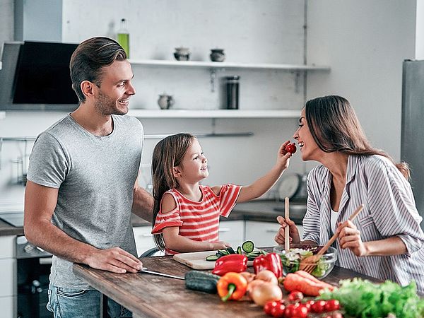 Eine junge glückliche Familie steht gemeinsam in der Küche und bereitet einen Salat zu