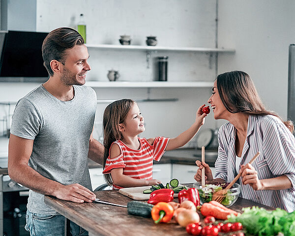 Eine junge glückliche Familie steht gemeinsam in der Küche und bereitet einen Salat zu