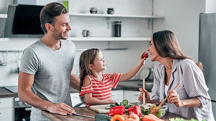 Eine junge glückliche Familie steht gemeinsam in der Küche und bereitet einen Salat zu