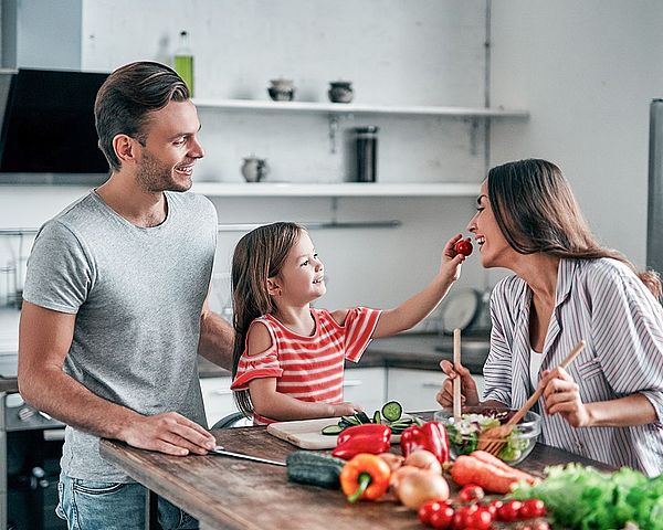 Eine junge glückliche Familie steht gemeinsam in der Küche und bereitet einen Salat zu