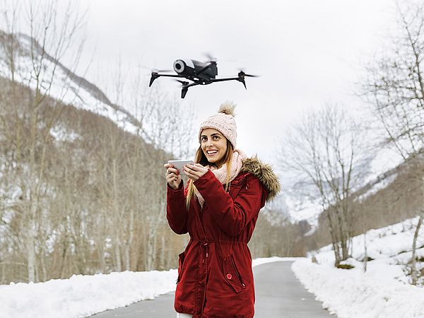 Eine junge Frau steuert lächelnd eine Drohne in einer Winterlandschaft.