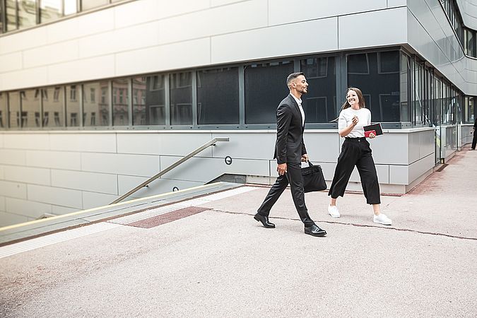 Ein junger Mann im Anzug und eine junge Frau in lockerer Business-Kleidung unterhalten sich während sie spazieren.