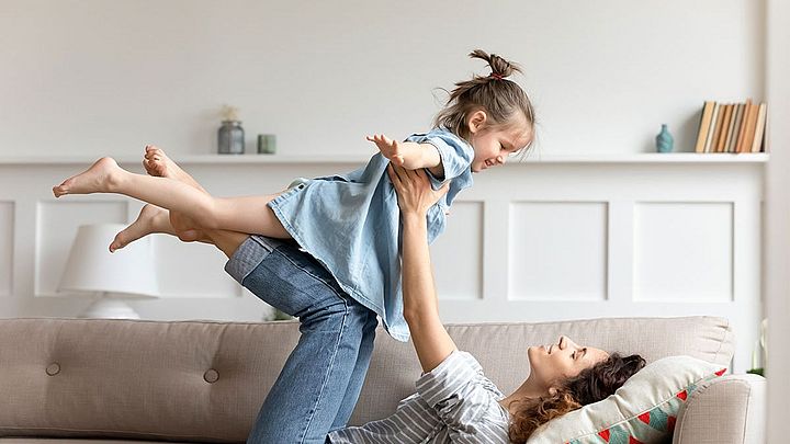 Mutter hebt kleine Tochter hoch. Das Kind streckt die Arme weg wie ein Flugzeug