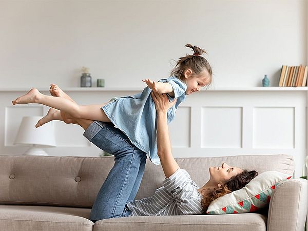 Mutter hebt kleine Tochter hoch. Das Kind streckt die Arme weg wie ein Flugzeug