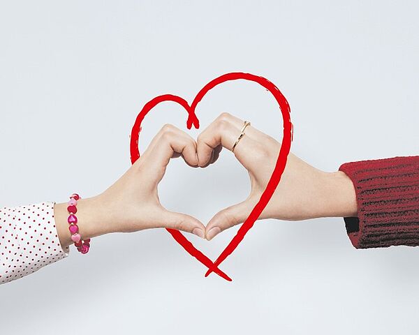 Zwei Personen formen mit ihren Händen gemeinsam ein Herz, das zusätzlich mit einer roten Linie nachgezeichnet ist.