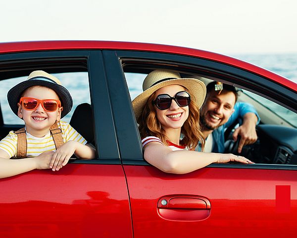 Eine glückliche Familie fährt mit dem Auto in den Urlaub. Die Eltern und das Kind schauen lächelnd aus den Fenstern.