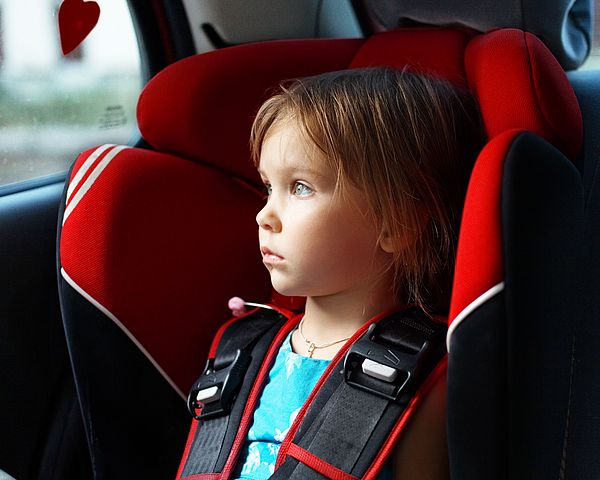 Kind in Kindersitz im Auto und schaut zum Fenster raus.
