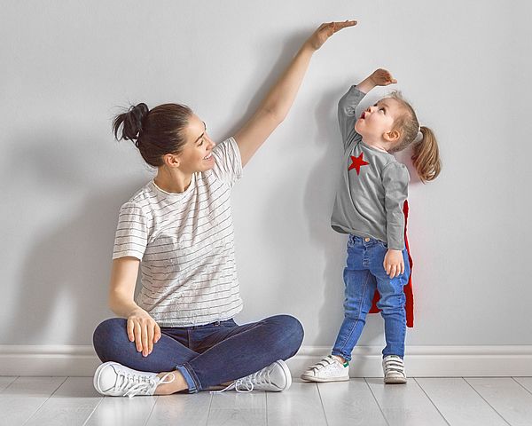 Mutter zeigt ihrer kleinen Tochter mit der Hand wie groß sie schon ist. 