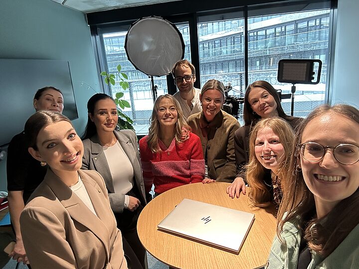 Gruppe von neun Personen steht um einen Tisch und macht ein Selfie.
