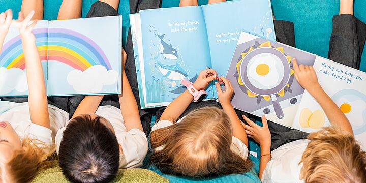 Bildaufnahme von oben, vier Kinder, die in bunten Büchern lesen.