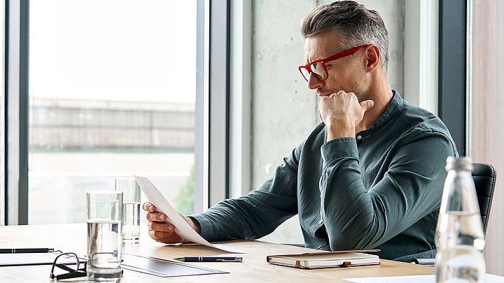 Ein Mann mit Brille liest konzentriert am Schreibtisch.