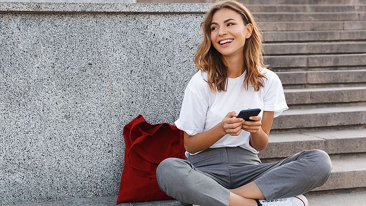 Eine junge Frau sitzt auf Treppen im Freien und tippt auf ihrem Smartphone.