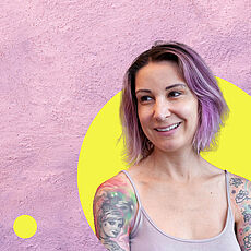 Porträt einer lächelnden Frau mit kurzen lilafarbenen Haaren und sichtbaren Tattoos an den Armen, vor rosafarbenem Hintergrund mit gelbem Kreis und grafischen Elementen.