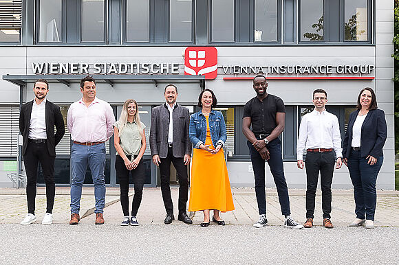 Viele Personen stehen vor einem Gebäude und lächeln in die Kamera.