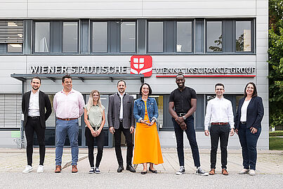 Viele Personen stehen vor einem Gebäude und lächeln in die Kamera.