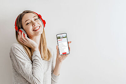 Eine junge Frau mit Kopfhörern hält ein Smartphone in die Kamera. Auf dem Smartphone ist die Onboarding App geöffnet