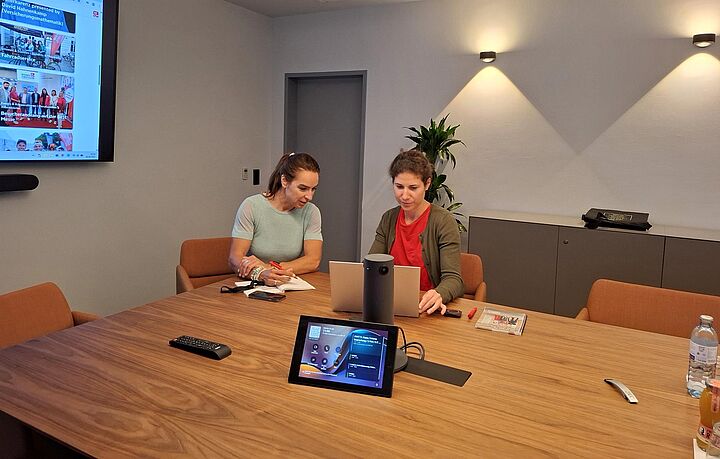 Zwei Personen sitzen vor einem Laptop in einem Besprechungsraum.