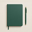 Ein grünes Notizbuch liegt auf einem weißen Tisch, daneben ein grüner Stift.