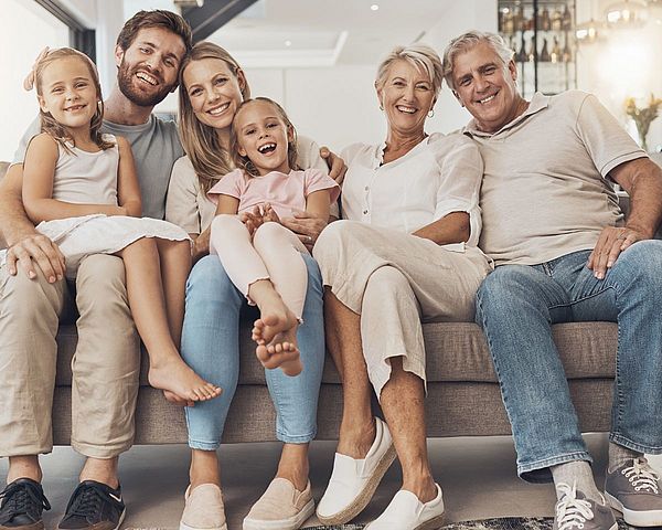 Drei Generationen Familie sitzen zusammen auf einem Sofa und sehen glücklich aus.