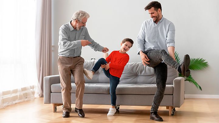 Drei glückliche Männer verschiedener Generationen tanzen im Wohnzimmer.
