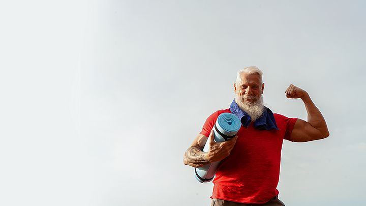 Ein muskulöser Senior posiert im Freien mit einer Gymnastikmatte in der Hand.