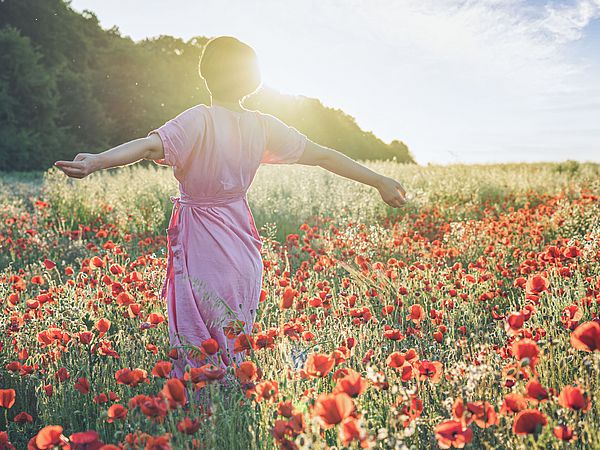 Frau in rosa Kleid läuft über ein Mohnblumenfeld.