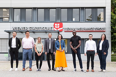 Mehrere Personen stehen vor einem Gebäude und blicken in die Kamera.