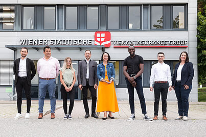 Mehrere Personen stehen vor einem Gebäude und blicken in die Kamera.