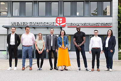 Mehrere Personen stehen vor einem Gebäude und blicken in die Kamera.