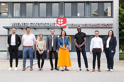 Mehrere Personen stehen vor einem Gebäude und blicken in die Kamera.