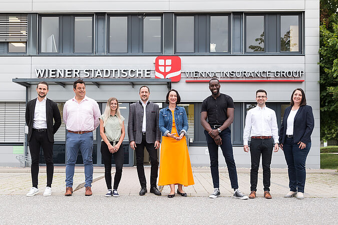 Mehrere Personen stehen vor einem Gebäude und blicken in die Kamera.