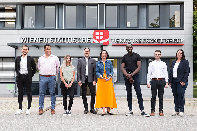 Mehrere Personen stehen vor einem Gebäude und blicken in die Kamera.