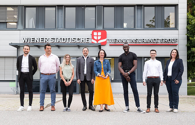 Mehrere Personen stehen vor einem Gebäude und blicken in die Kamera.