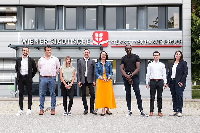 Mehrere Personen stehen vor einem Gebäude und blicken in die Kamera.