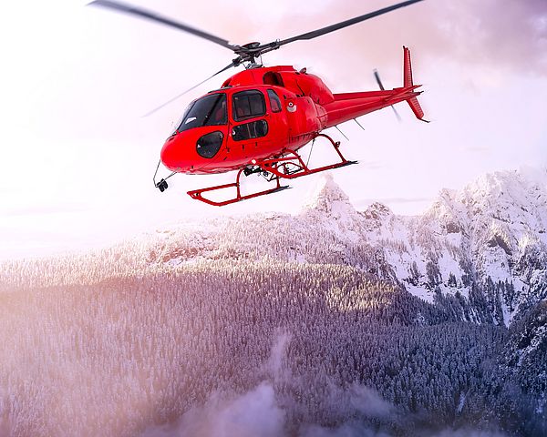 Ein Helikopter fliegt über verschneiten Bergen.
