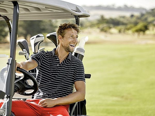 Glücklicher Mann fährt mit seinem Golfcart über den Golfplatz.