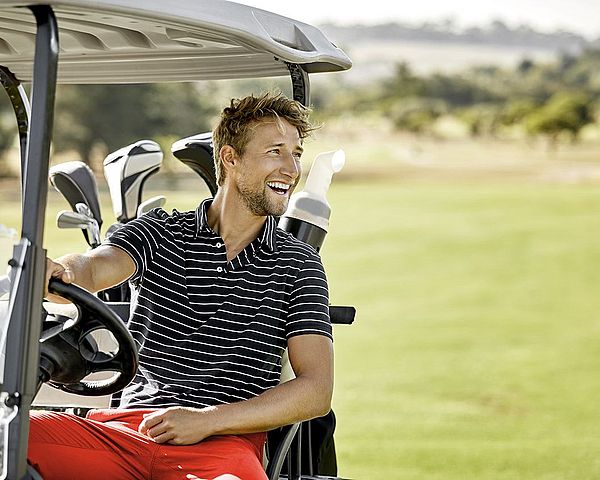Ein glücklicher Mann fährt mit seinem Golfcart über den Golfplatz.