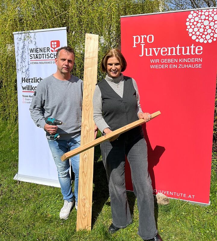 Ein Mann und eine Frau stehen vor zwei Roll-Ups und sind dabei, zwei Holzpfade zusammenzuschrauben.