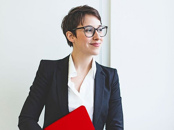 Eine Geschäftsfrau mit Brille hält ihren Laptop und lächelt dabei