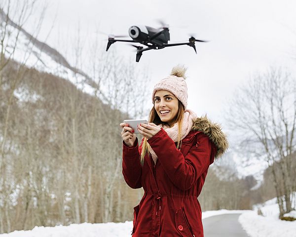 Eine junge Frau steuert lächelnd eine Drohne in einer Winterlandschaft.