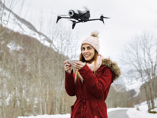 Eine junge Frau steuert lächelnd eine Drohne in einer Winterlandschaft.