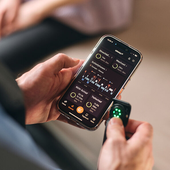 Zwei Männerhände halten ein Handy, auf dem Daten zum Schlaf zu lesen sind.