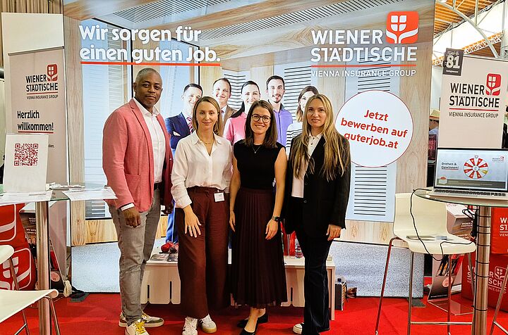 Auf dem Bild sieht man 1 Mann und 3 Frauen im Businessoutfit vor einem einem Messestand