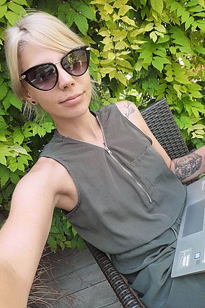 Raffaella Lang, ein Lehrling bei der Wiener Städtischen, sitzt in eleganter Kleidung vor einem Laptop und lächelt mit Sonnenbrille in die Kamera